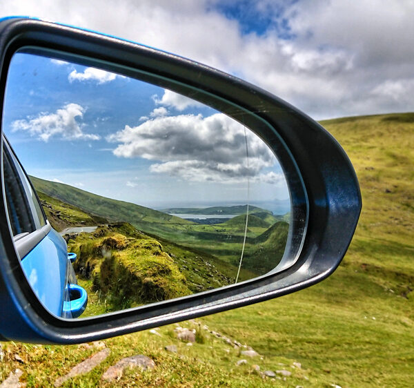 Kijkend door een rearview spiegel op de auto op een panorama van een landschap met weelderige groene velden en weiden